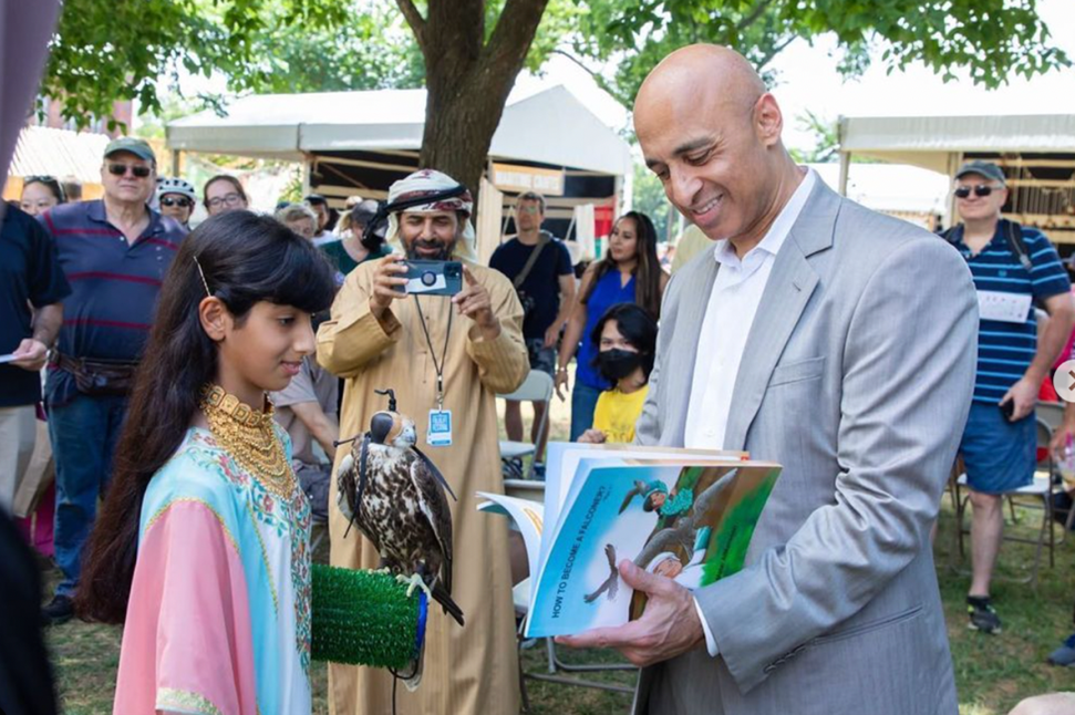 UAE Ambassador reads a children's book next to a young girl holding a trained falcon